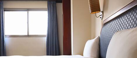 A hotel room with a large bed, a window with curtains, and a wall-mounted lamp.