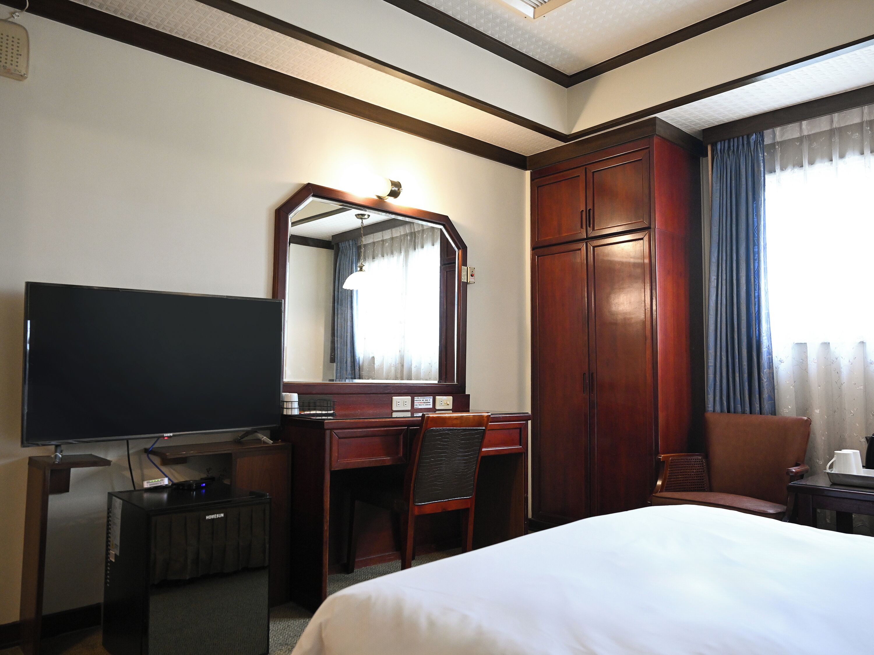 A hotel room with a bed, a desk with a chair, a television, and a wardrobe.