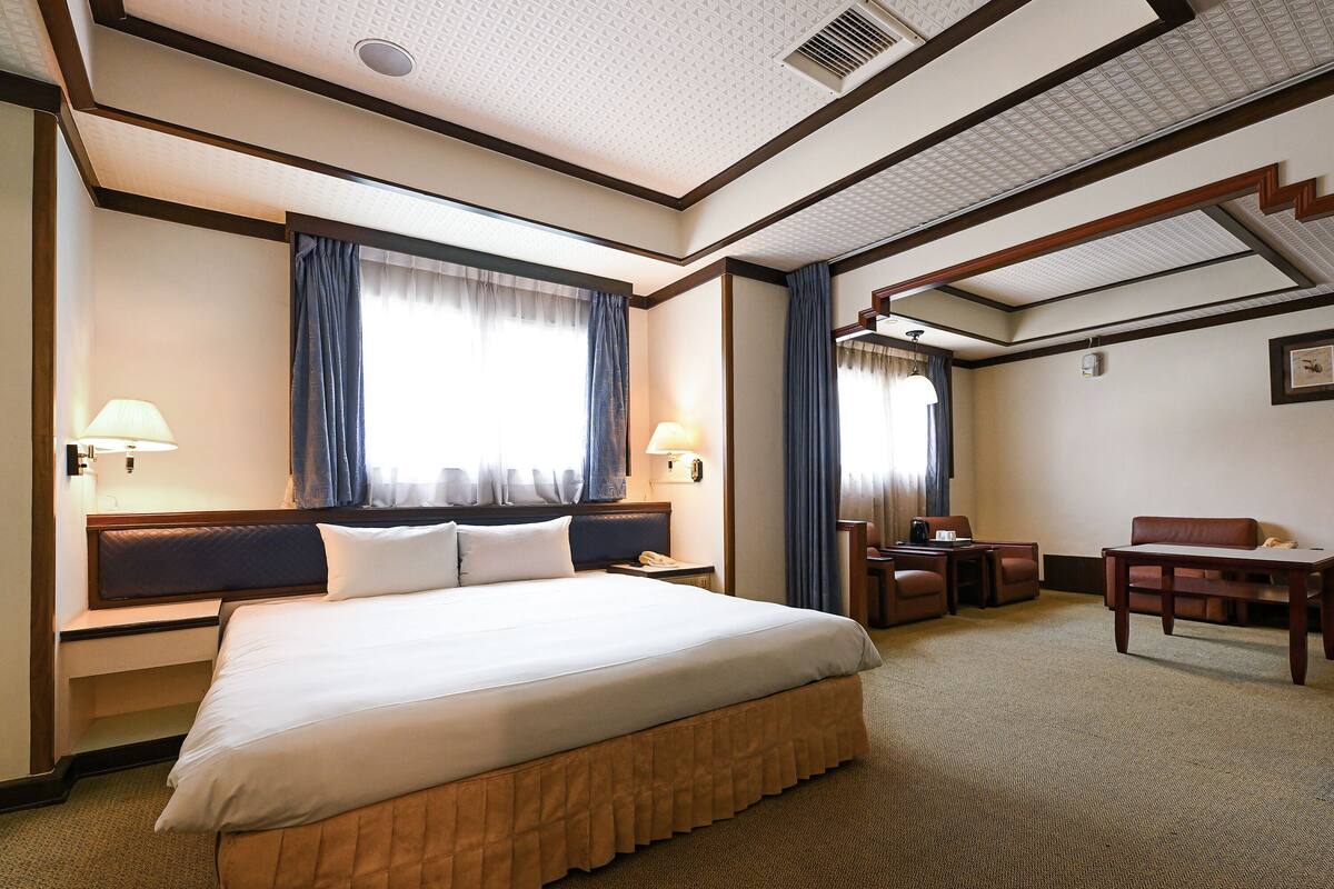 A hotel room with a large bed, two bedside tables, a desk, and a chair.