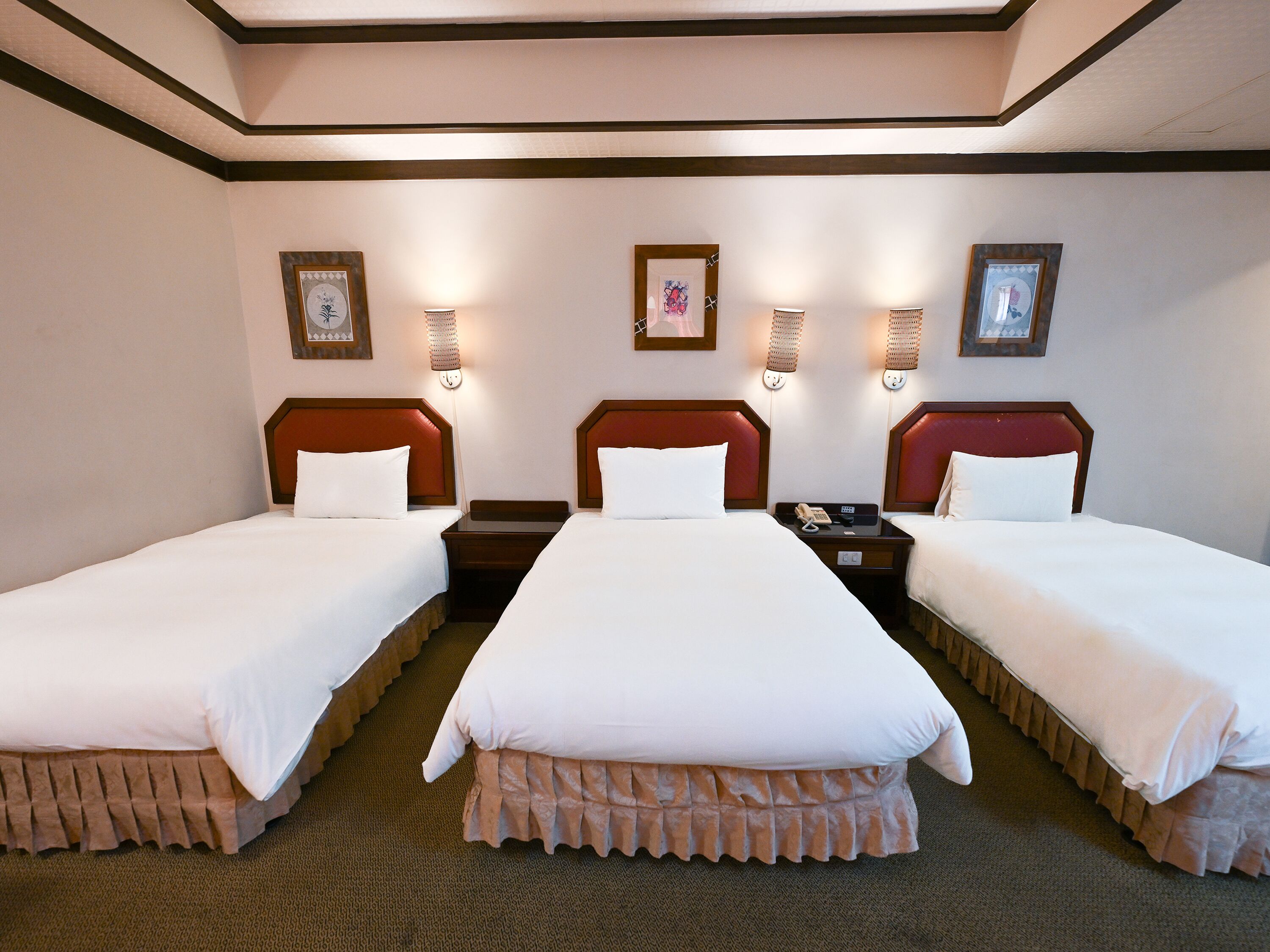 A hotel room with two beds, a nightstand, a telephone, and wall-mounted lamps.