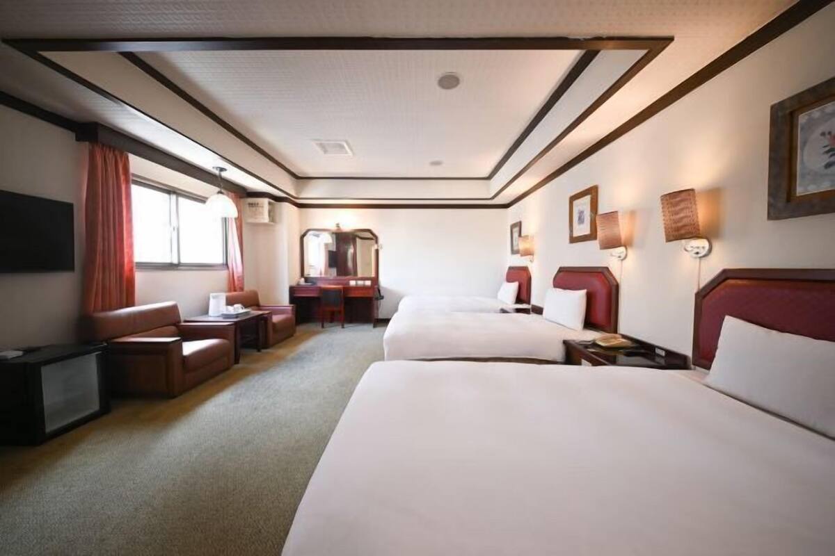 A hotel room with two beds, a desk, a chair, a TV, and a window with curtains.