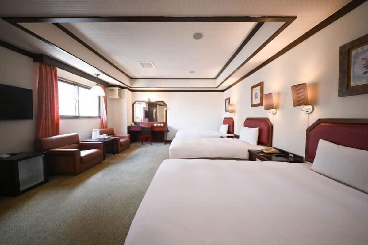 A hotel room with two beds, a desk, a chair, a TV, and a window with curtains.