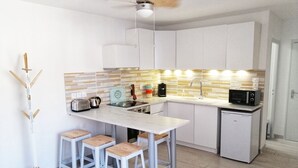 A modern kitchen with white cabinets, a marble countertop, and a small refrigerator.