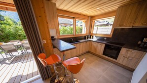 A modern kitchen with wooden cabinets, a black countertop, and a large window overlooking a deck. - NEW Garden 7 person Apartment with Hot Tub, next to Super Morzine (Morzine)