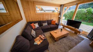 A modern living room with a sectional sofa, a wooden coffee table, and a TV on a wooden stand. - NEW Garden 7 person Apartment with Hot Tub, next to Super Morzine (Morzine)