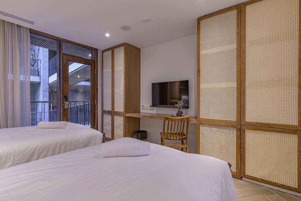 A hotel room with two beds, a TV mounted on the wall, and a wooden desk.