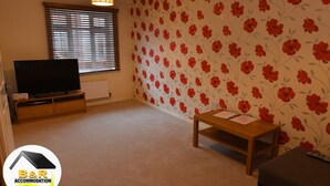 A room with a television on a wooden stand, a small wooden table, and a floral wallpaper. - ⭐B and R Serviced Accommodation and Apartments Amesbury⭐ Archer house  (Amesbury)
