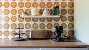 Una cocina con tostadora, cafetera y una estantería con utensilios de cocina.