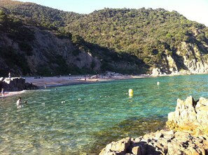 Una playa costera con aguas cristalinas, formaciones rocosas y un paisaje montañoso al fondo.