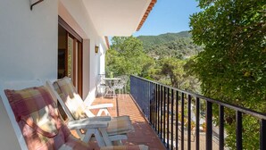 Un balcón con sillones blancos y una mesa, con vista a un paisaje montañoso.