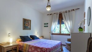 Un dormitorio con cama, mesita de noche, lámpara y ventana con cortinas.