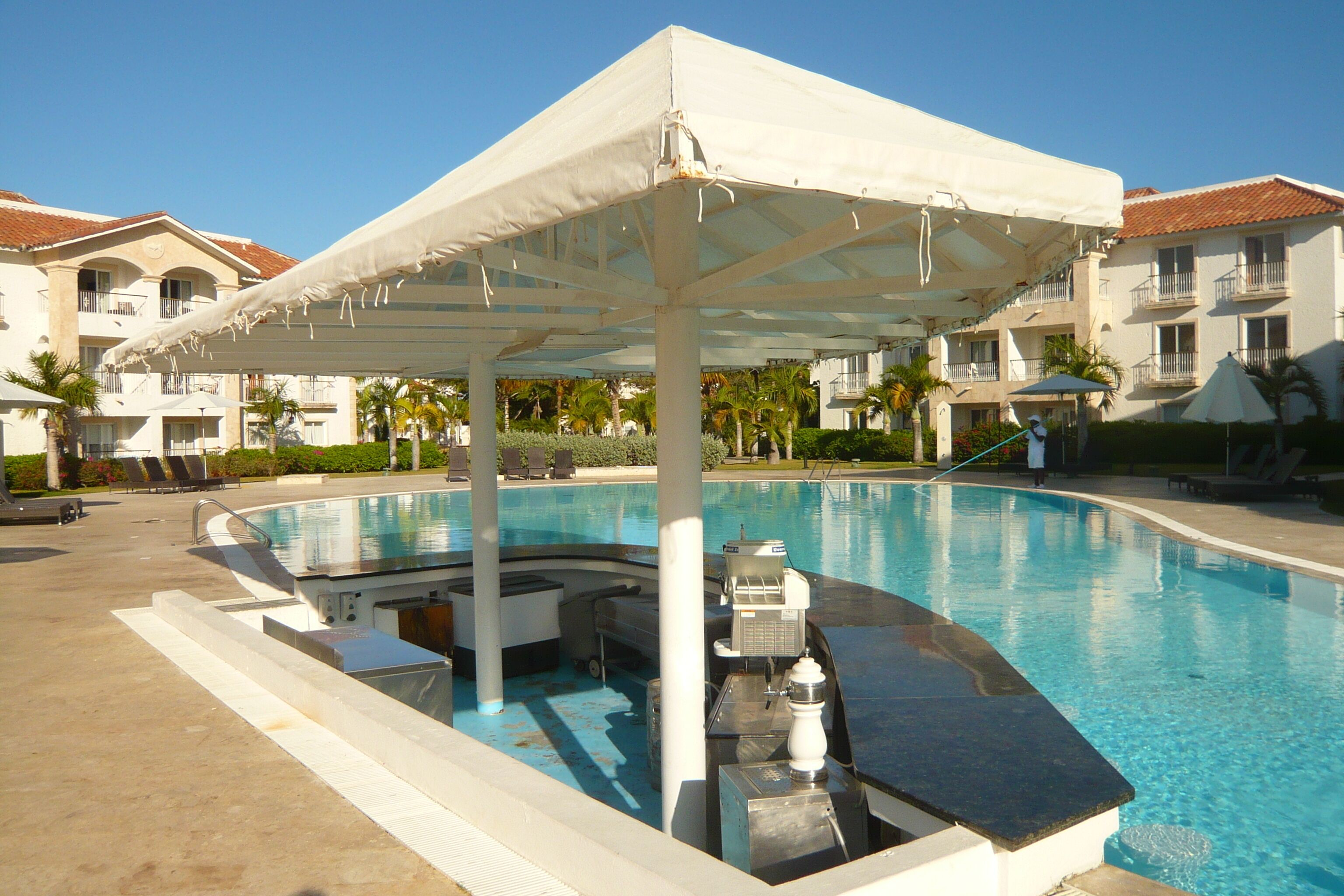 Piscina com área coberta, cadeiras de espreguiçadeira e bar à beira da piscina.