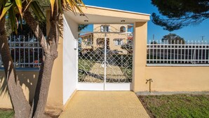 A gated entrance with a metal gate, a small covered area, and a paved path leading to the gate. - Pine Trees Apartment (Preveza)