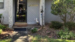 A two-story house with a grey exterior, a front door, and a small garden area with a tree and some shrubs. - Spacious quiet 3BR townhome Five minutes to beach (St. Simons Island)