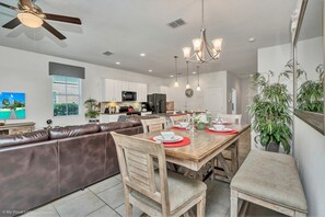 Una cocina moderna con armarios blancos, una zona de comedor con una mesa y sillas de madera, y un sofá de cuero marrón.