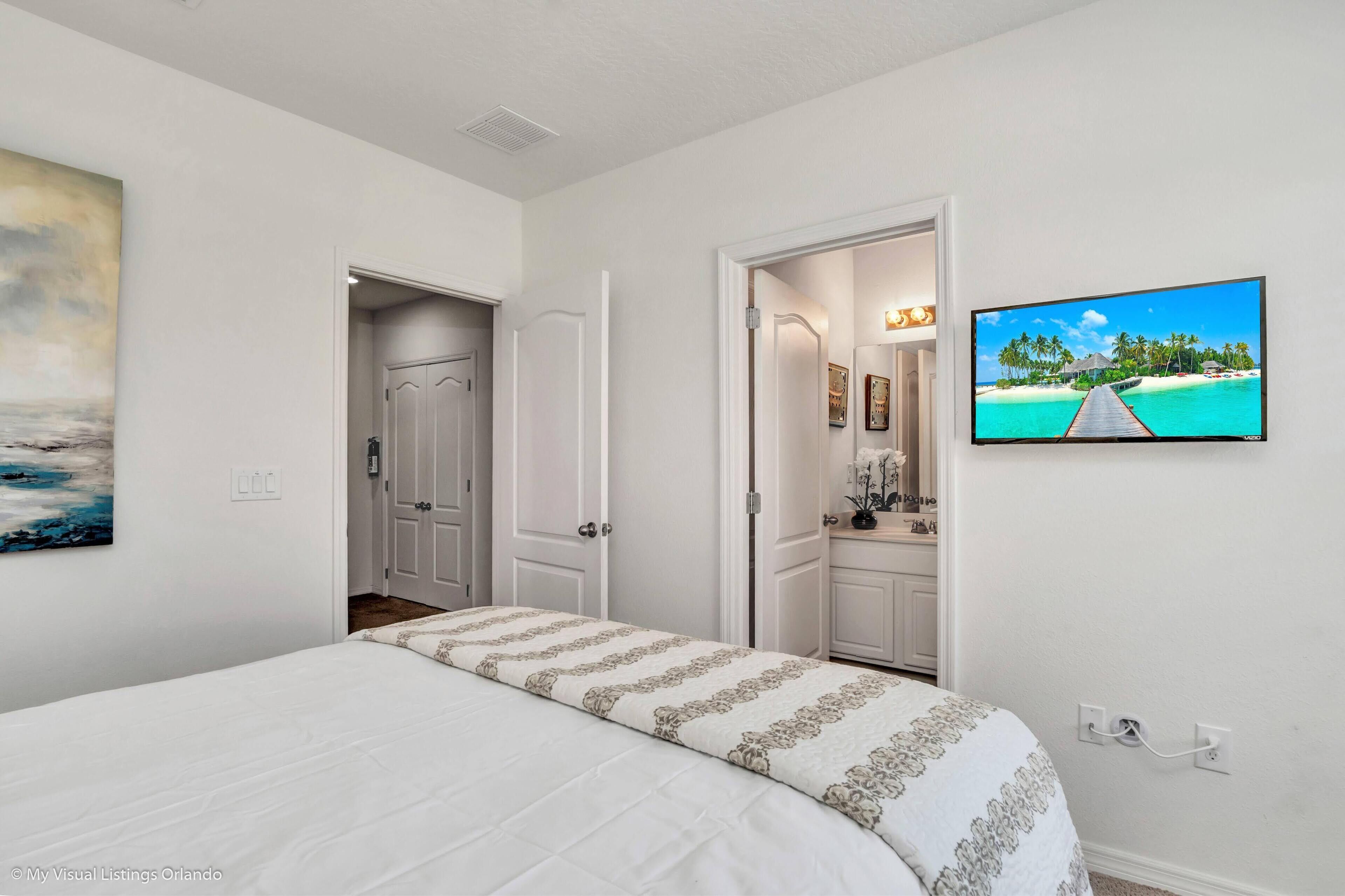 Un dormitorio con una cama, un cuadro, un televisor y una puerta que da a un baño.
