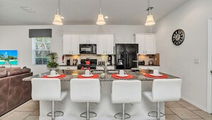 A modern kitchen with white cabinets, a central island with bar stools, stainless steel appliances, and pendant lighting.