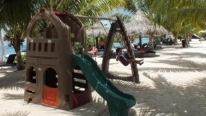 Ein Spielplatz am Strand mit Rutsche und Schaukeln.