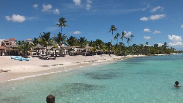 Una playa con agua turquesa cristalina, palmeras y cabañas.