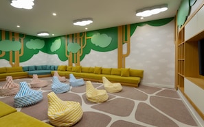 A children's play area with a green wall, a yellow sofa, and striped bean bags. - Rixos Water World Aktau (Aktau)