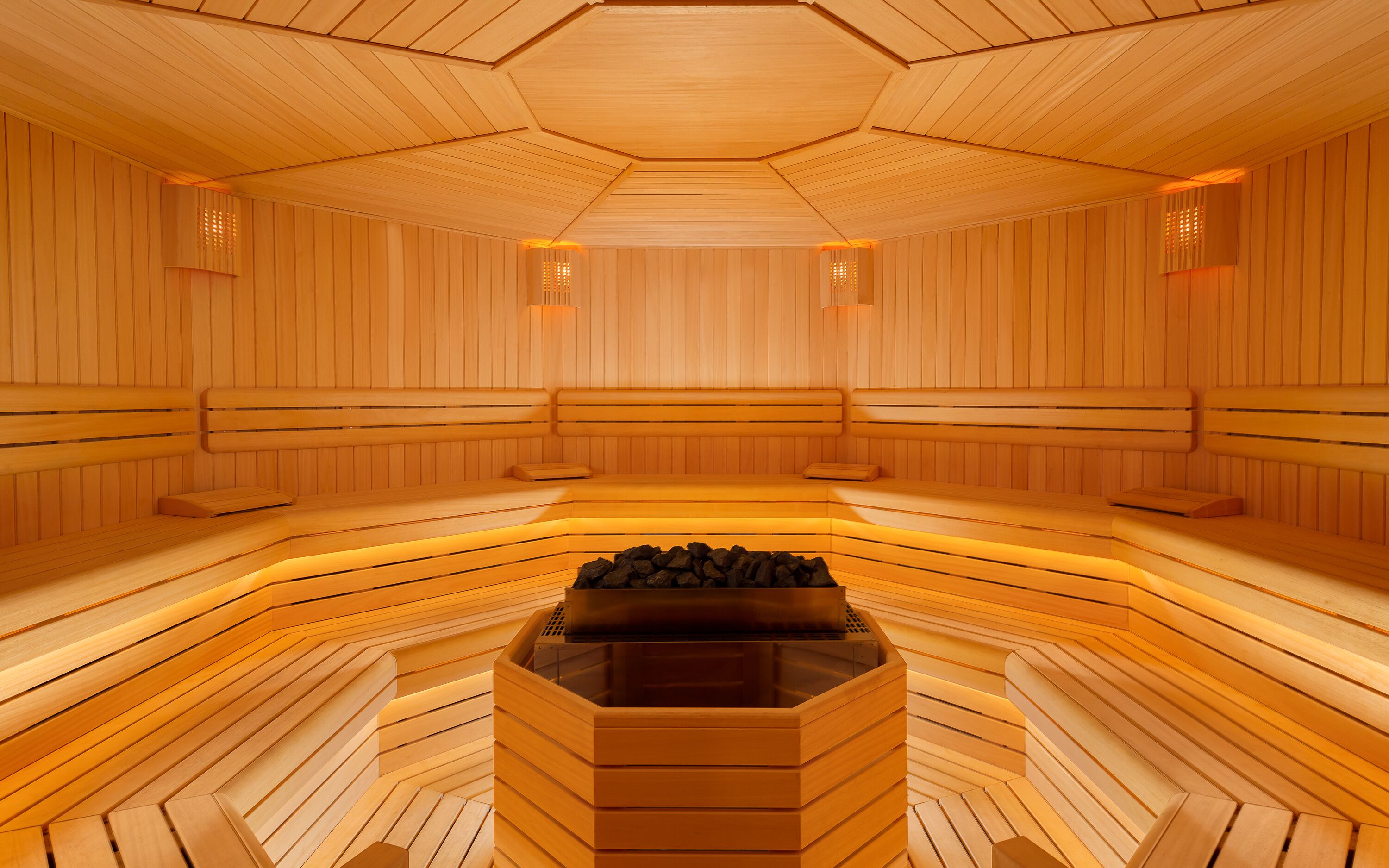 A sauna with wooden benches arranged in a semi-circular pattern around a central heated stone area.