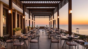 An outdoor dining area with tables and chairs, a wooden pergola, and a view of the sea. - Rixos Water World Aktau (Aktau)
