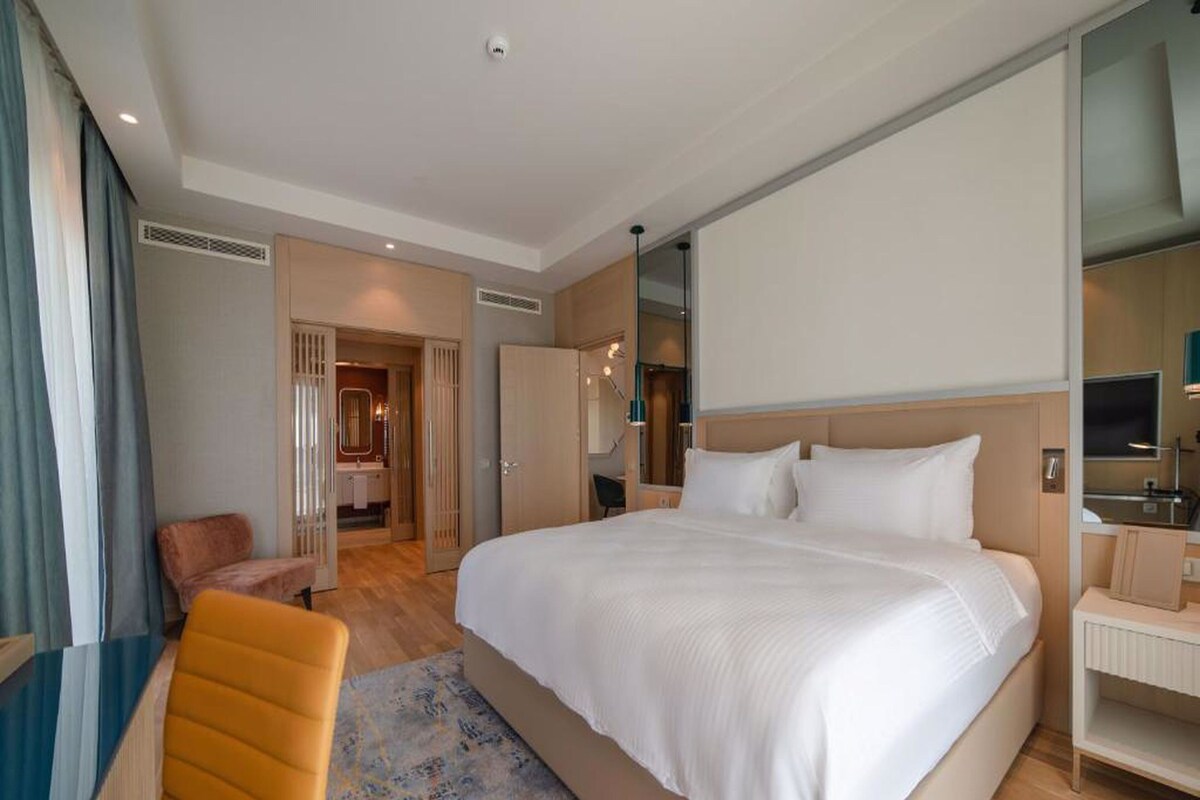 A hotel room with a large bed, a desk, a chair, and a bathroom visible through an open door.