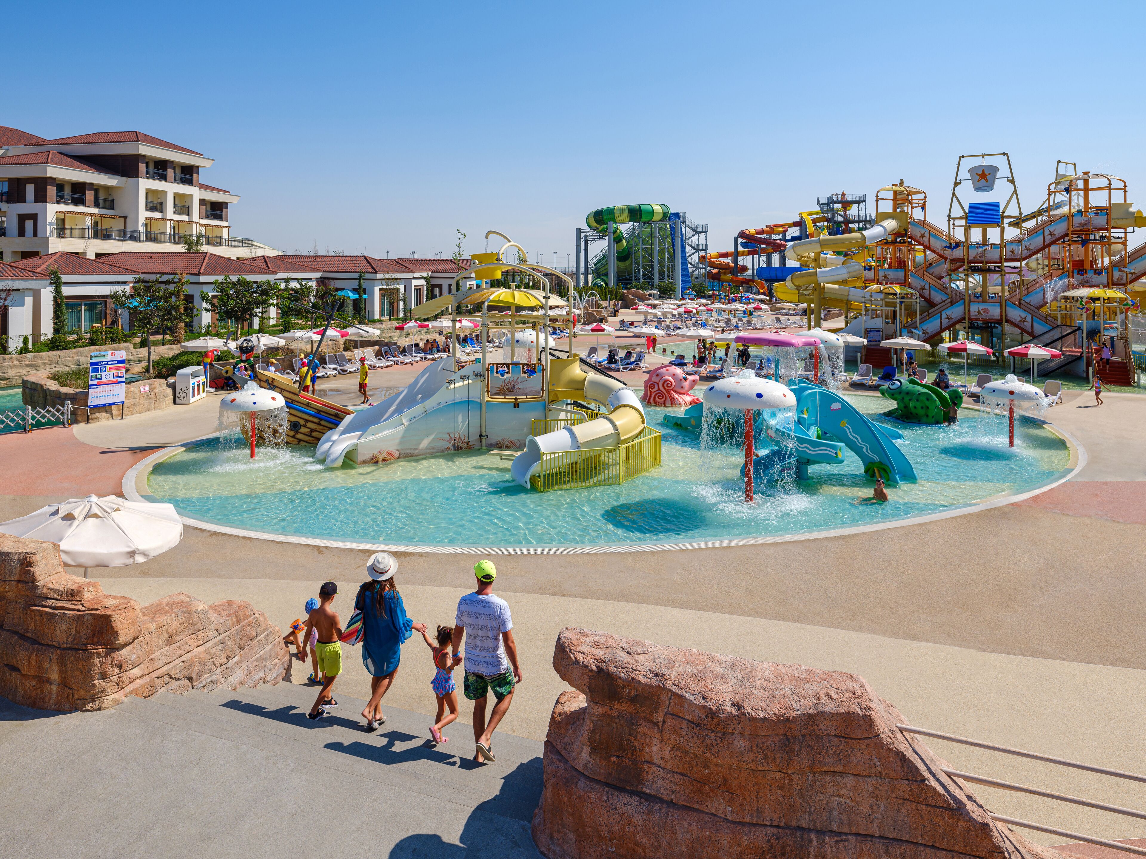 A water park with various slides and play areas, surrounded by a pool and lounge chairs.