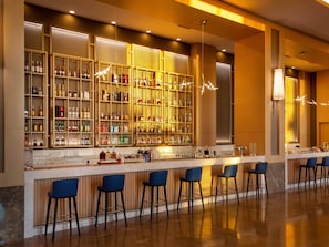 A bar area with a long counter, multiple stools, and shelves stocked with bottles. - Rixos Water World Aktau (Aktau)