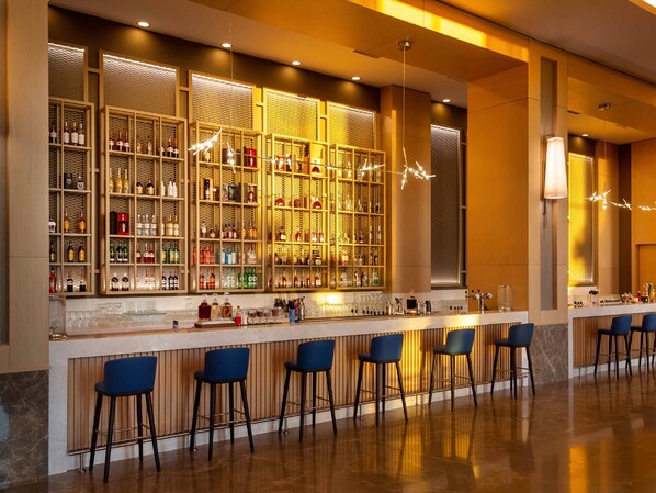 A bar area with a long counter, multiple stools, and shelves stocked with bottles. - Rixos Water World Aktau (Aktau)