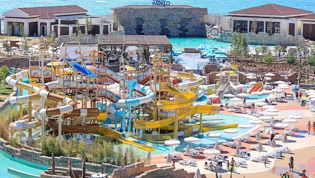 A water park with multiple slides and pools, a large rock formation labeled 'WATER WORLD,' and a beach area with sun loungers. - Rixos Water World Aktau (Aktau)
