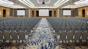A conference room with rows of chairs, a large screen, and a patterned carpet. - Rixos Water World Aktau (Aktau)
