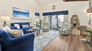 A living room with a blue sofa, armchairs, a coffee table, and a large window with a view of a building.