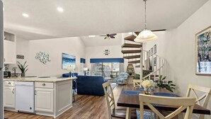 A modern kitchen with white cabinetry, a wooden dining table, and a spiral staircase leading to a balcony.