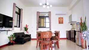 A dining area with a round table, chairs, a sofa, a TV, and a fan. - Eliza Inn (Magong)