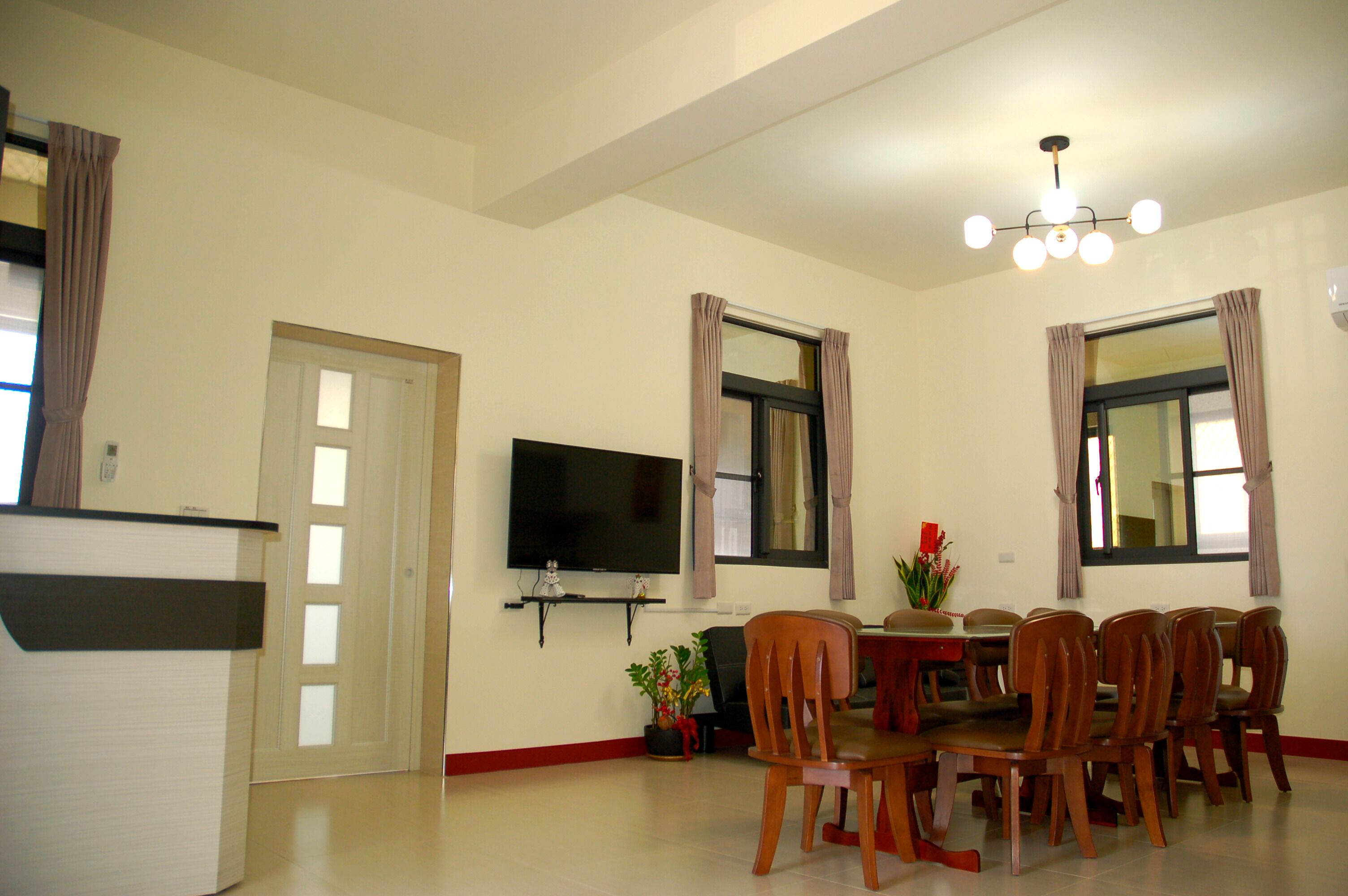 A dining area with a table and chairs, a flat-screen TV mounted on the wall, and a ceiling light fixture.
