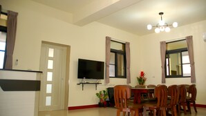A dining area with a table and chairs, a flat-screen TV mounted on the wall, and a ceiling light fixture. - Eliza Inn (Magong)