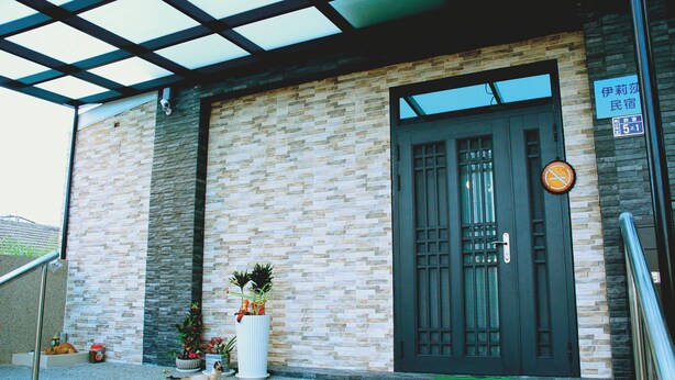 A building with a tiled facade, a dark door with a window, and a sign indicating a room number. - Eliza Inn (Magong)