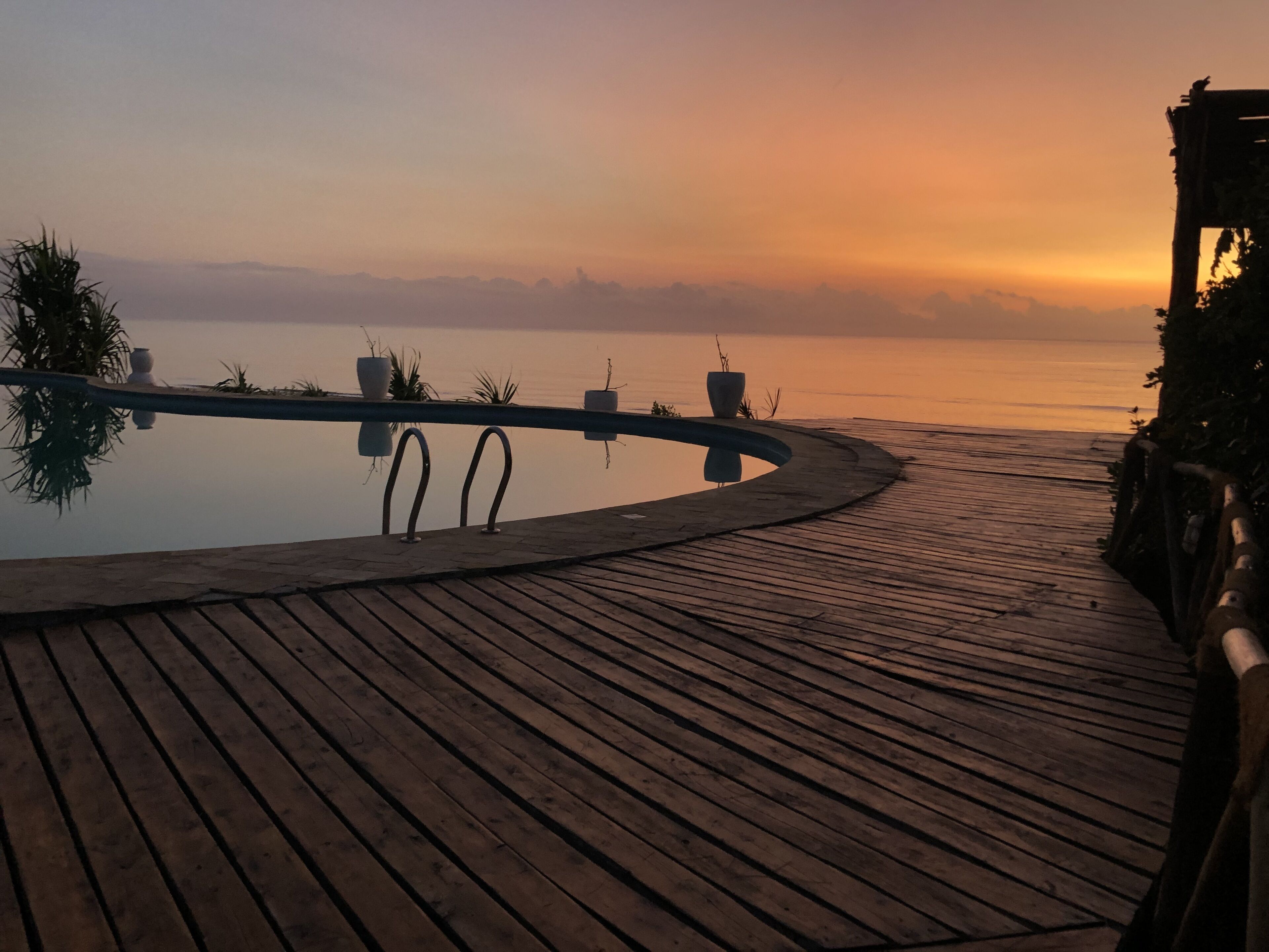 Een houten terras dat leidt naar een zwembad met uitzicht op de ondergaande zon.
