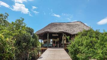 A wooden walkway leading to a thatched-roof structure with benches and a sign.
