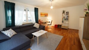 Uma sala de estar moderna com um sofá cinzento, uma mesa de centro branca e um chão de madeira.