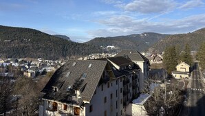 A multi-story building with a sloped roof, likely a hotel or residential complex, surrounded by a mountainous landscape and a clear sky. - Cozy 2-Bedroom Apartment with Balcony & Free Parking in Villard-de-Lans (Villard-de-Lans)