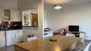 A modern kitchen with white cabinets, a dishwasher, and a dining area with a wooden table and white chairs. - Cozy 2-Bedroom Apartment with Balcony & Free Parking in Villard-de-Lans (Villard-de-Lans)