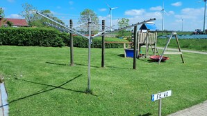 A playground with a swing set and a slide, a small playhouse, and a sign that reads "FEWO". - Vacation apartment "Auf der Warf" (Wittmund)