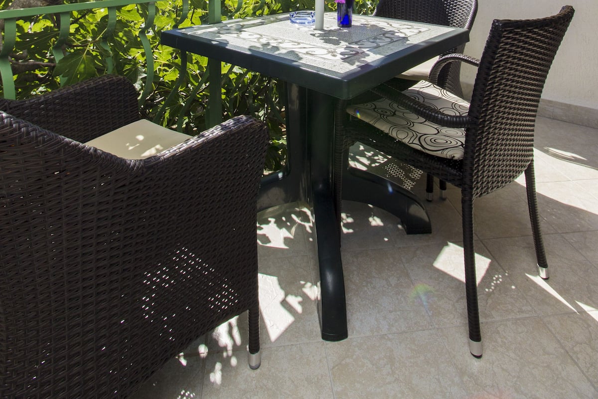 Un patio al aire libre con una mesa, sillas, un paraguas azul y un jarrón con flores moradas.