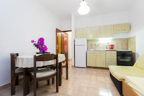 A compact kitchen with wooden cabinets, a refrigerator, and a dining area with a table and chairs. - 7 Olives Apartments (Rogoznica)
