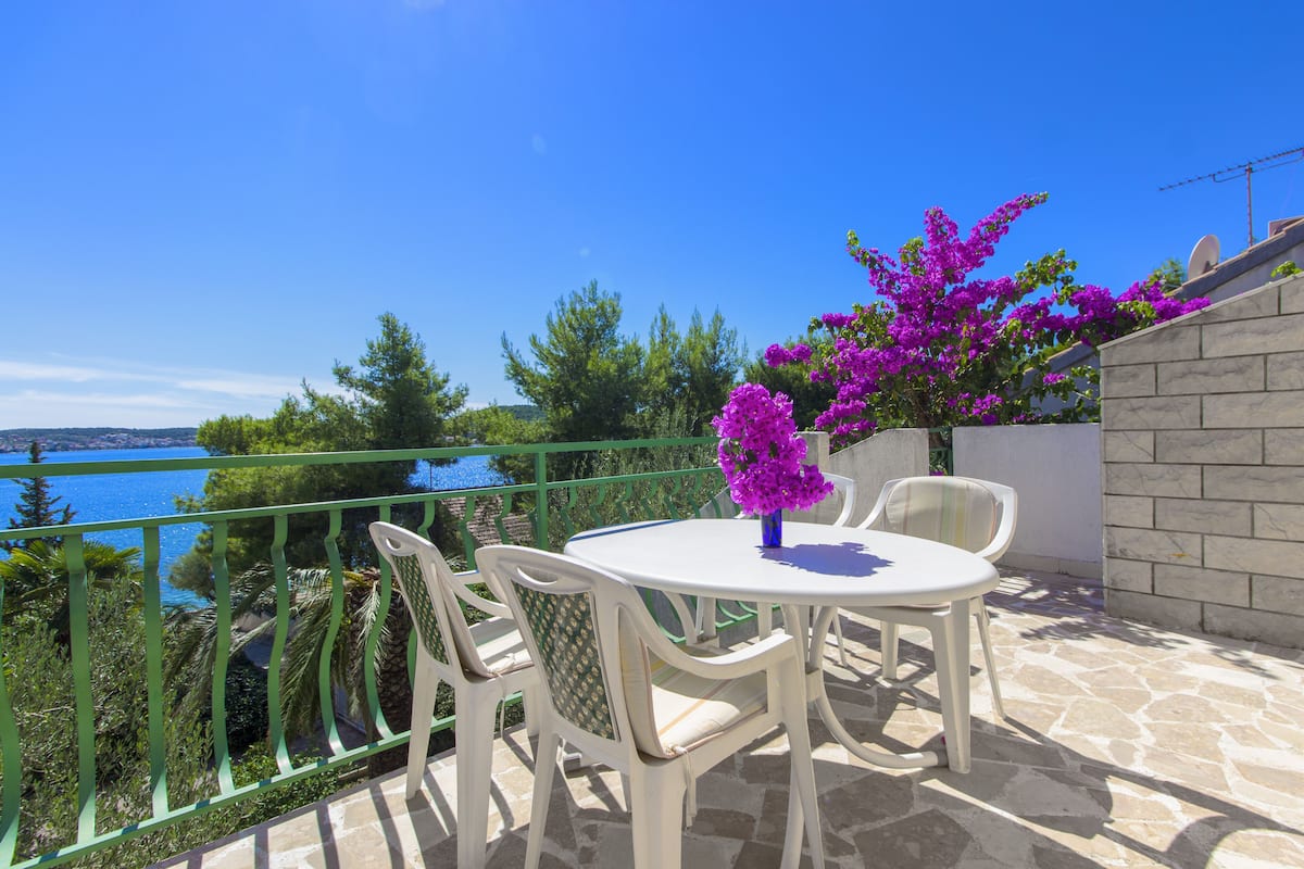 Una terraza con una mesa y sillas, con vista a un cuerpo de agua y follaje.