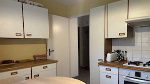 Una cocina compacta con armarios blancos, una mesa redonda de madera y un horno empotrado.