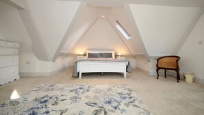 Un dormitorio con techo inclinado, una cama, lámparas de noche, un aparador, una silla y una alfombra con estampado floral.