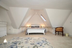 A bedroom with a sloped ceiling, a bed, bedside lamps, a dresser, a chair, and a floral carpet. - The Quays Christchurch Dorset (Christchurch)